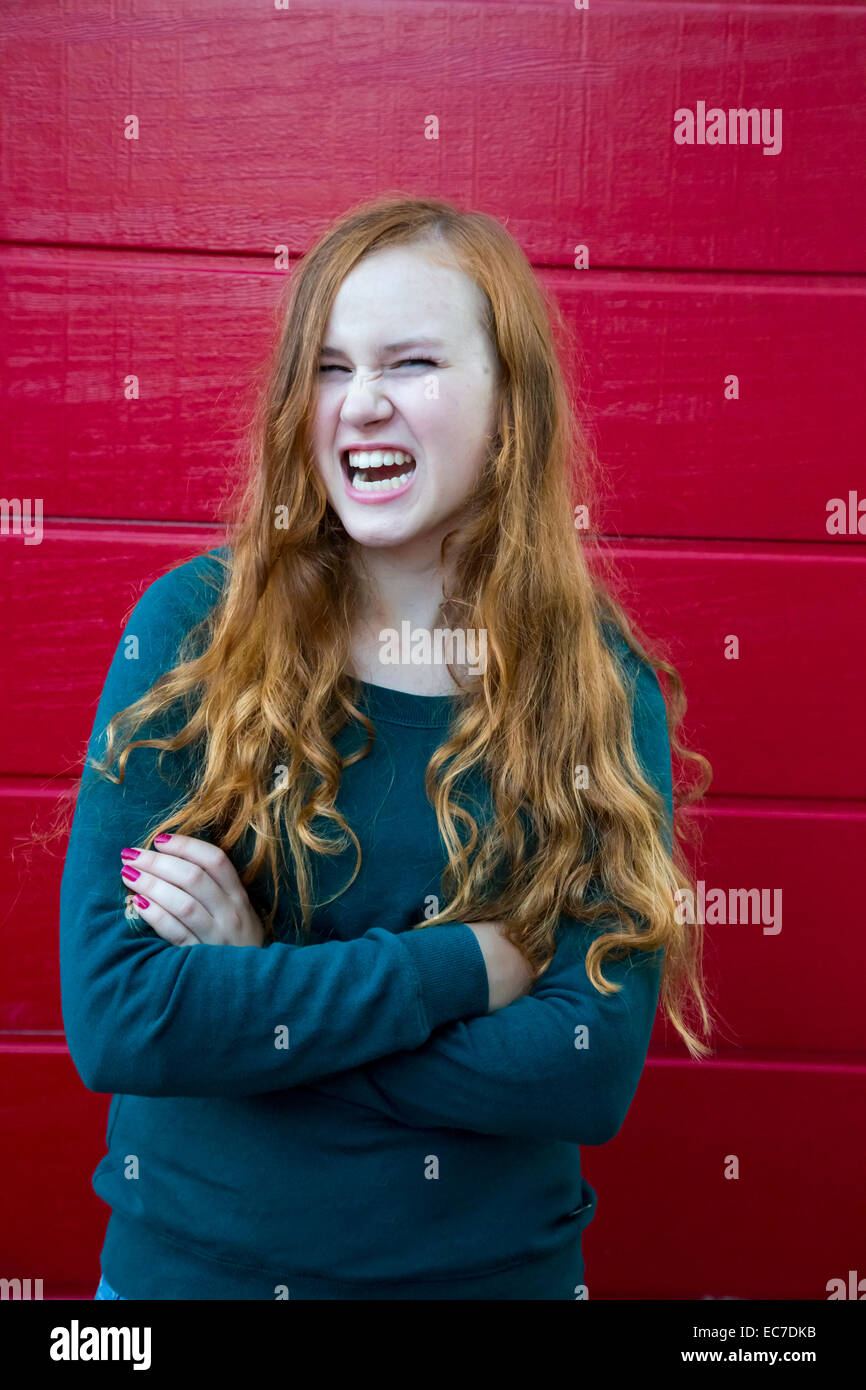 Portrait of angry teenage girl with crossed arms in front of red wooden ...
