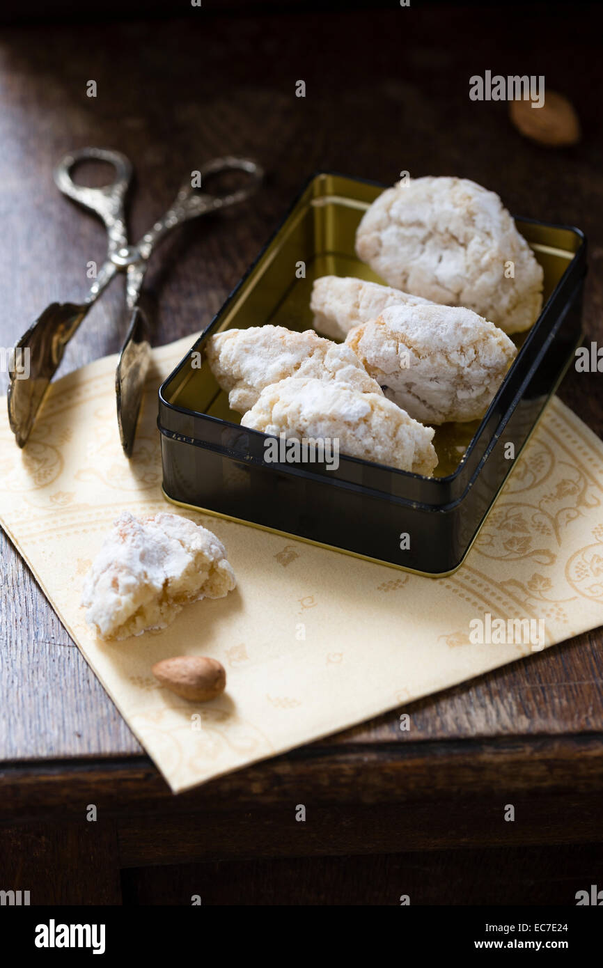 Cookie tin of Ricciarelli and pastry tong on napkin and dark wood Stock Photo