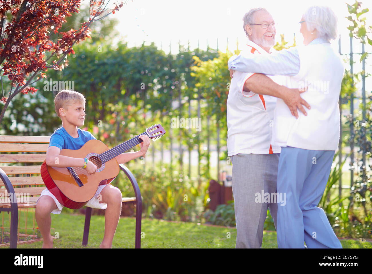 Senior couple dancing in park with grandson playing guitar Stock Photo