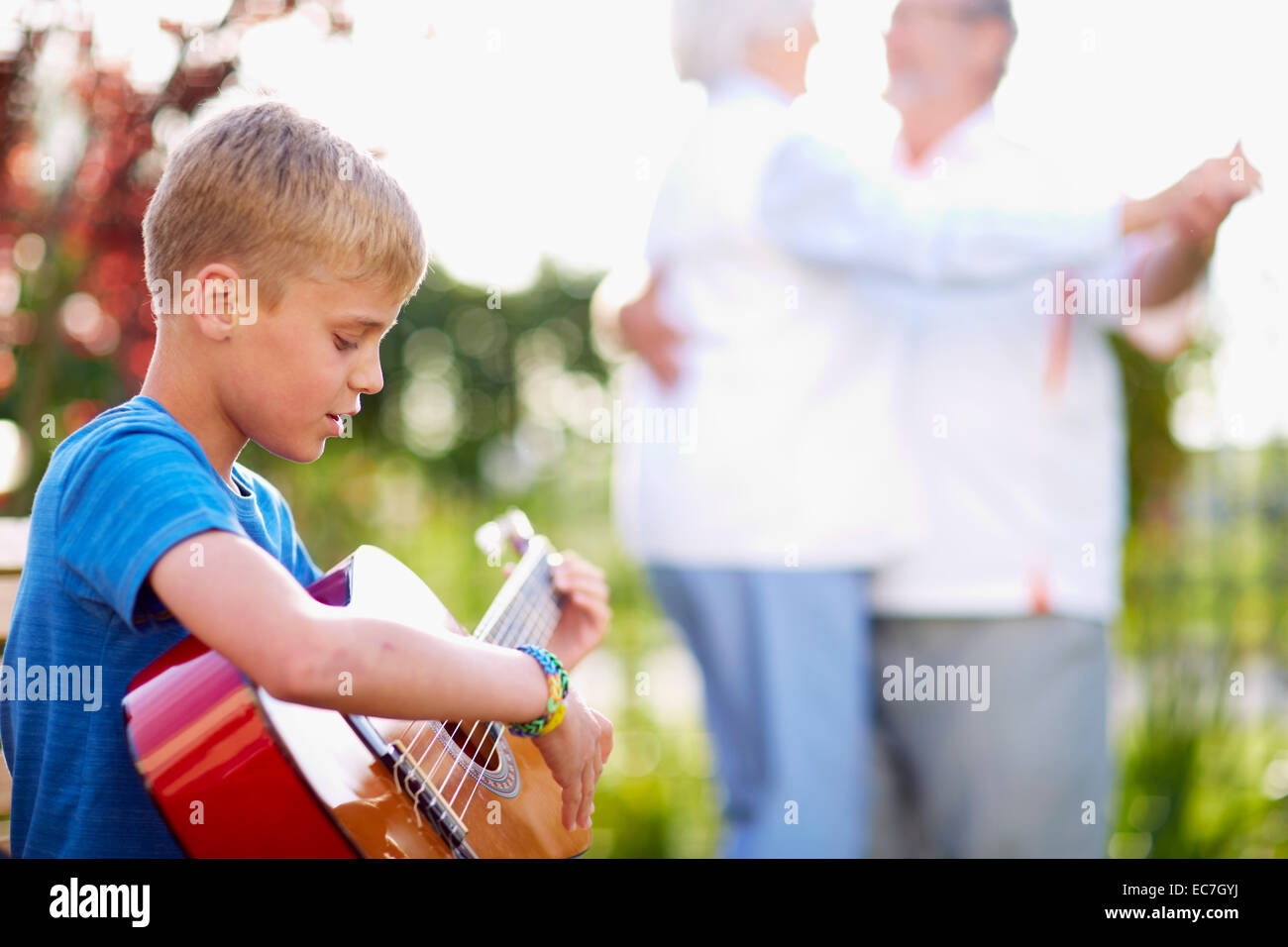 Grandson playing guitar with senior couple dancing in park Stock Photo