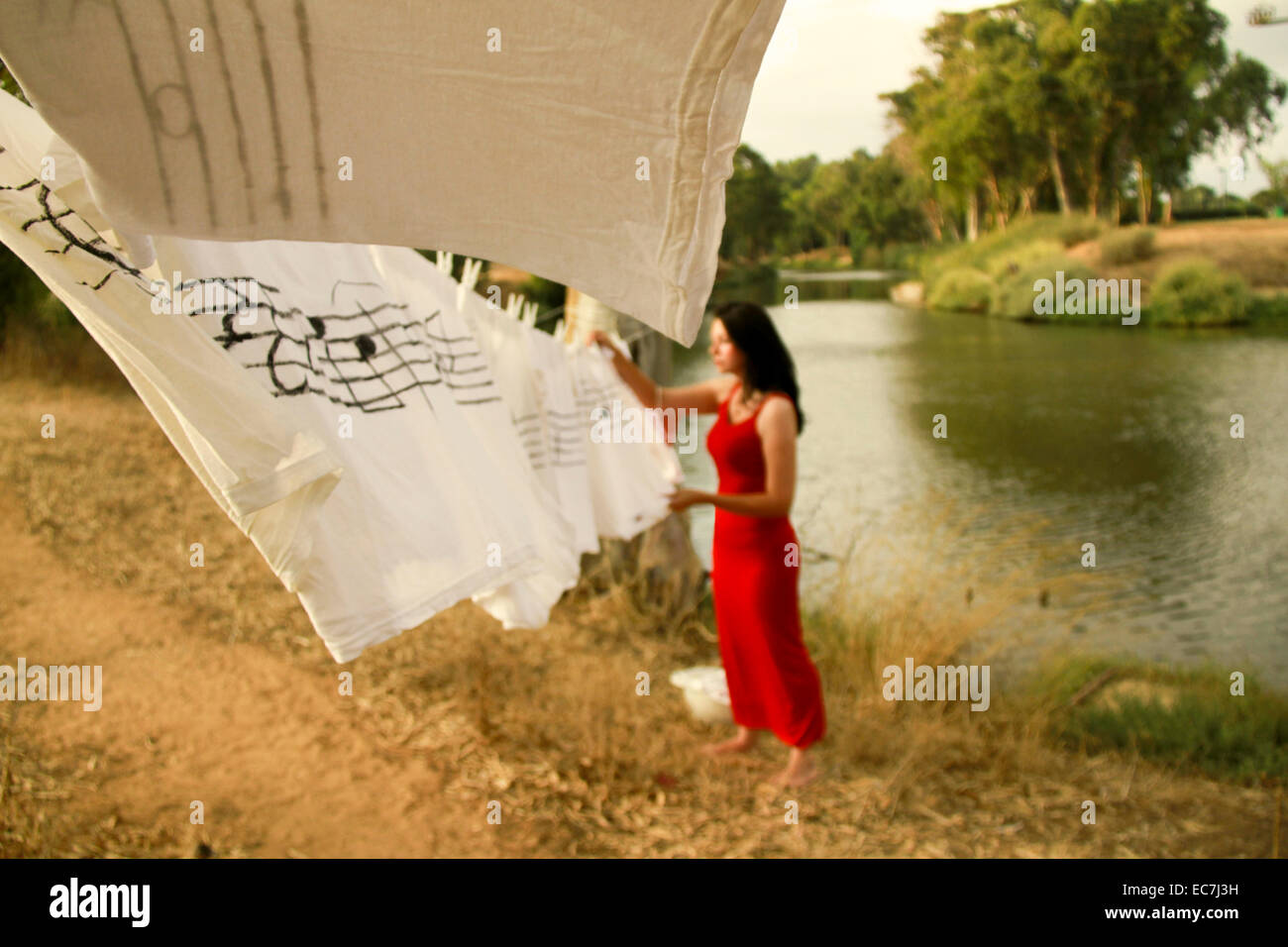 back to nature concept Woman in red dress hangs up washing on the riverbank Stock Photo