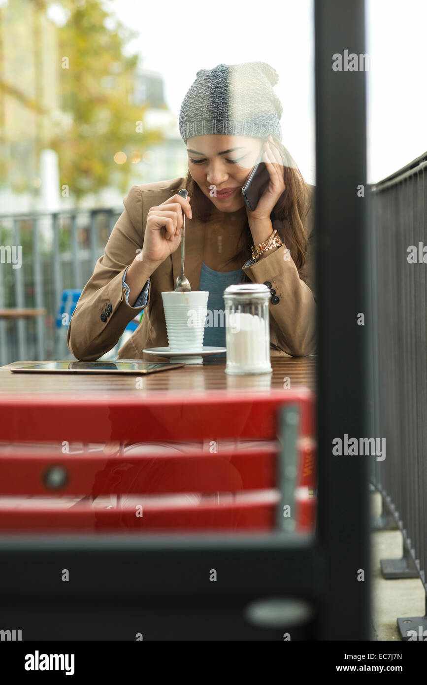 Young woman sitting at sidewalk cafe telephoning with smartphone Stock Photo