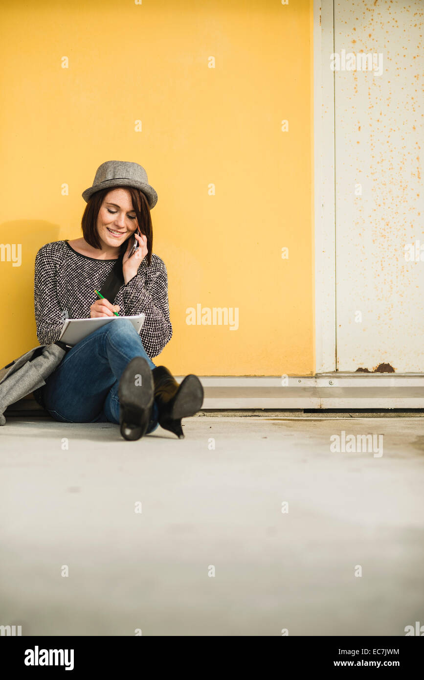 Young woman sitting on floor with notebook and cell phone Stock Photo
