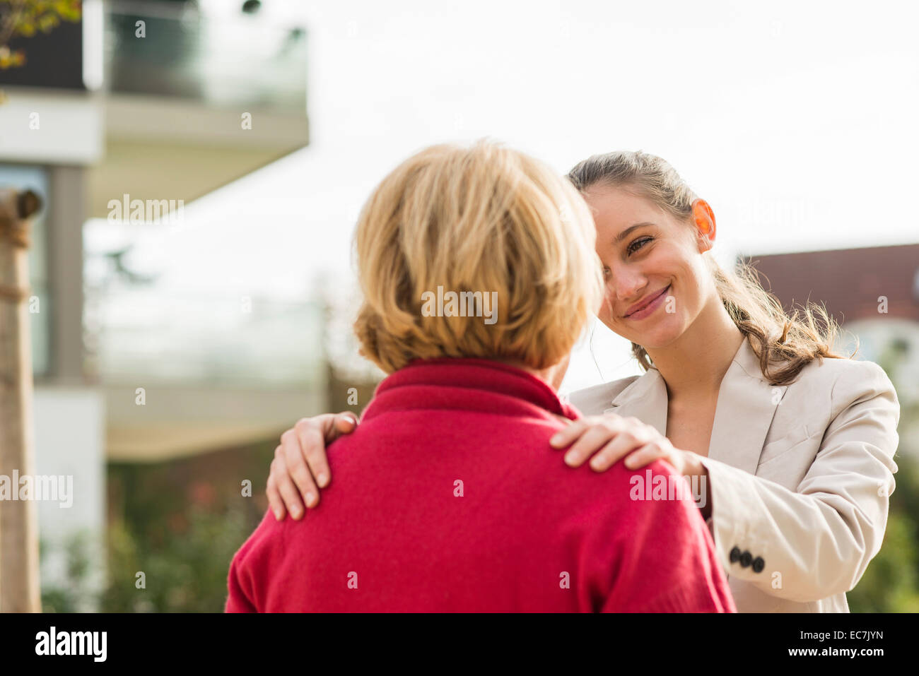 Smiling young woman with hands on shoulders of her grandmother Stock Photo