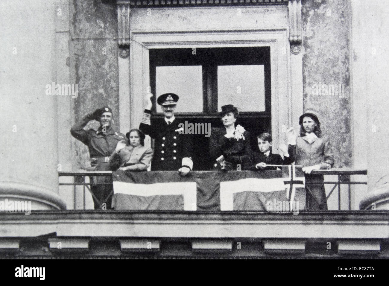 Photograph of the Norwegian Royal Family including King Haakon Crown, Crown Prince Olav and Prince Harald waving from the balcony of Oslo's Palace. Dated 1945 Stock Photo