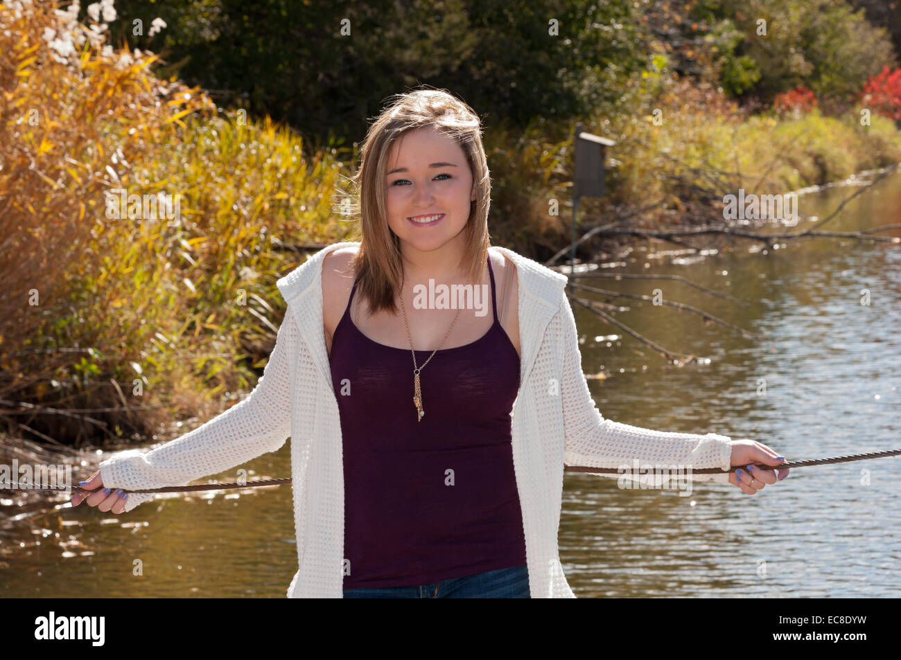 Outdoor portrait of young woman leaning against lake pier in autumn Stock Photo