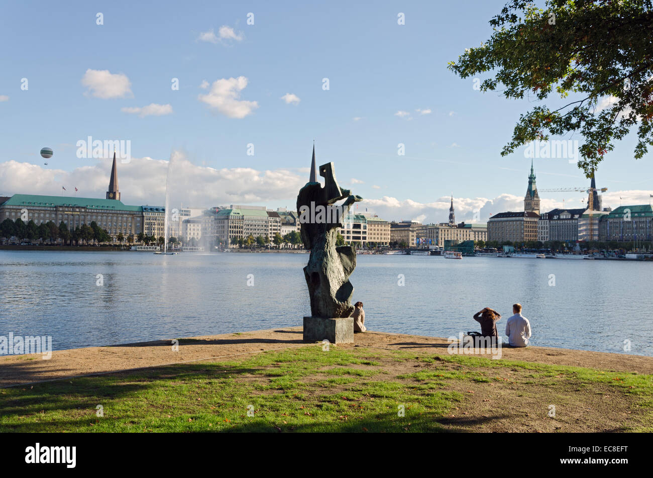 HAMBURG, GERMANY - SEPTEMBER 26: A group of young people seated next to a sculpture at the edge of Lake Alster on September 26, Stock Photo