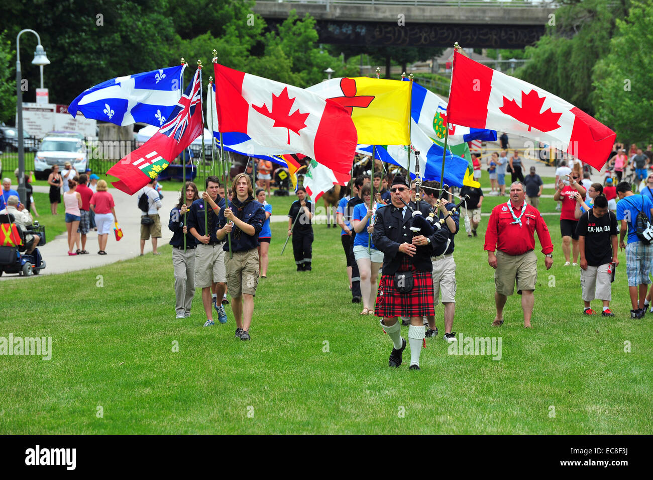 A bagpiper leads a precession of Canadian flags at a Canada Day celebration held in park in London, Ontario. Stock Photo