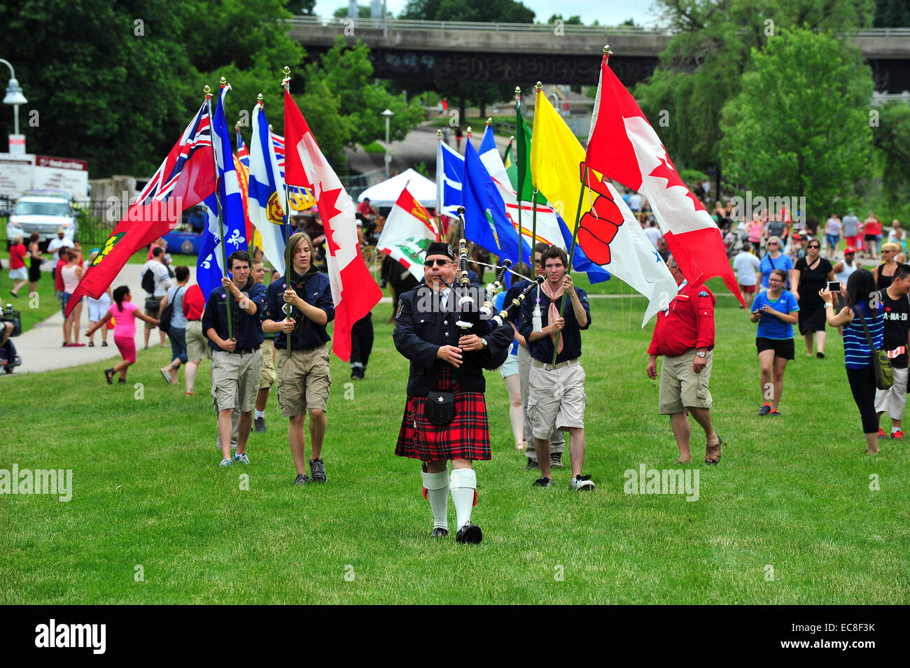 A bagpiper leads a precession of Canadian flags at a Canada Day celebration held in park in London, Ontario. Stock Photo