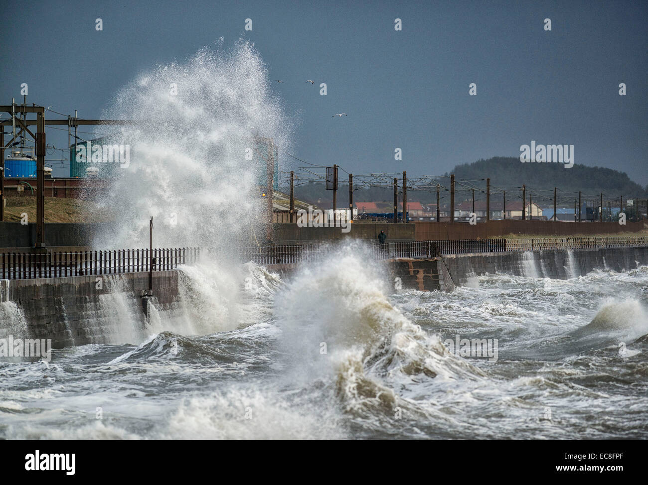 Men dodge the waves as they crash over the promenade wall on December 10, 2014 in Saltcoats, Scotland. Stock Photo