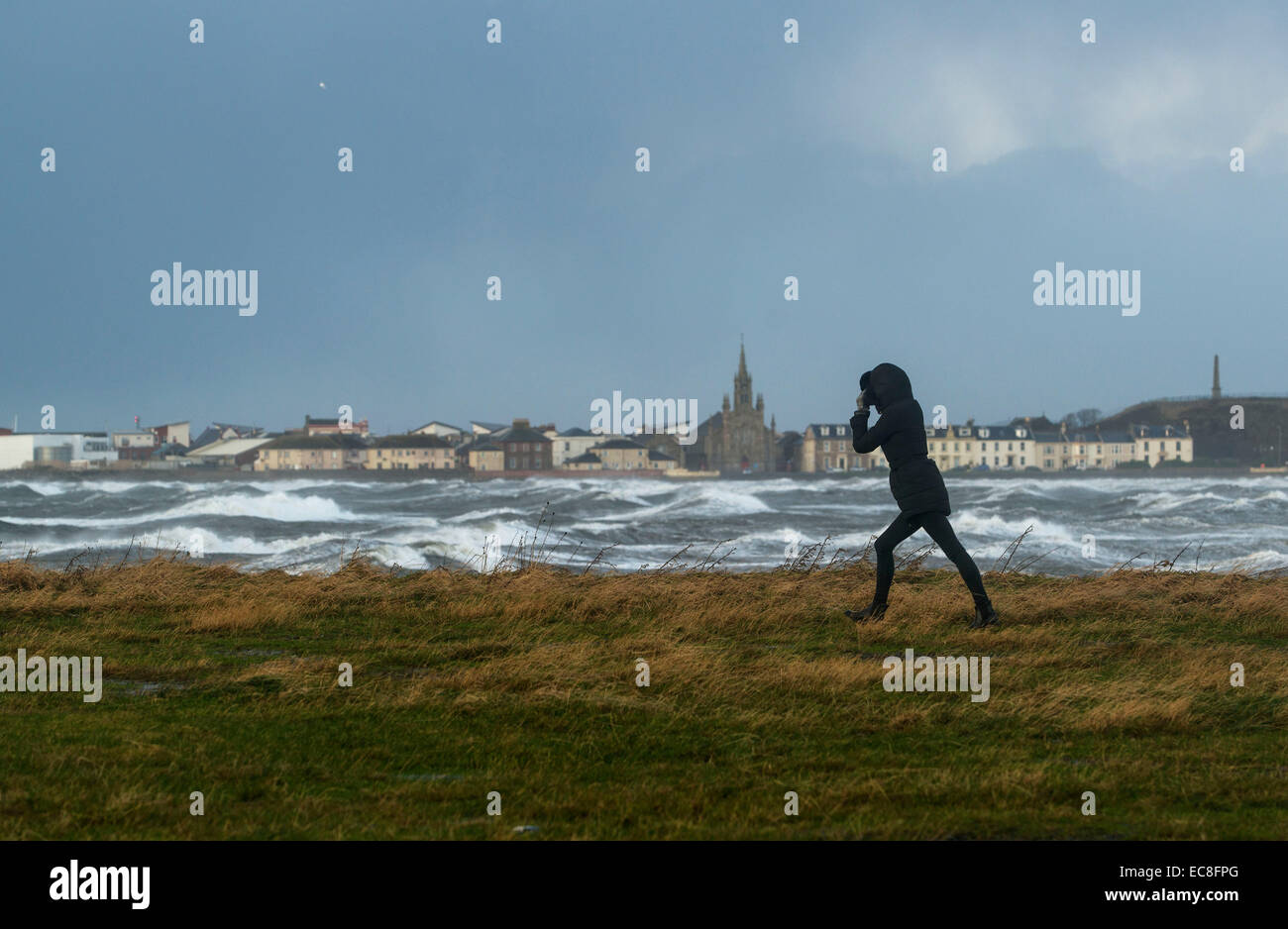A woman walks along the coast as the waves crash over the promenade wall on December 10, 2014 in Saltcoats, Scotland. Stock Photo
