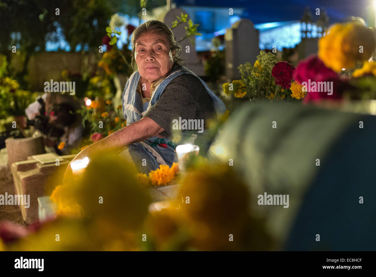An elderly woman reflects at the gravesite of a relative at Xoxocatian cemetery decorated with flowers and candles for the Day of the Dead Festival known in spanish as D’a de Muertos on October 31, 2014 in Oaxaca, Mexico. Stock Photo