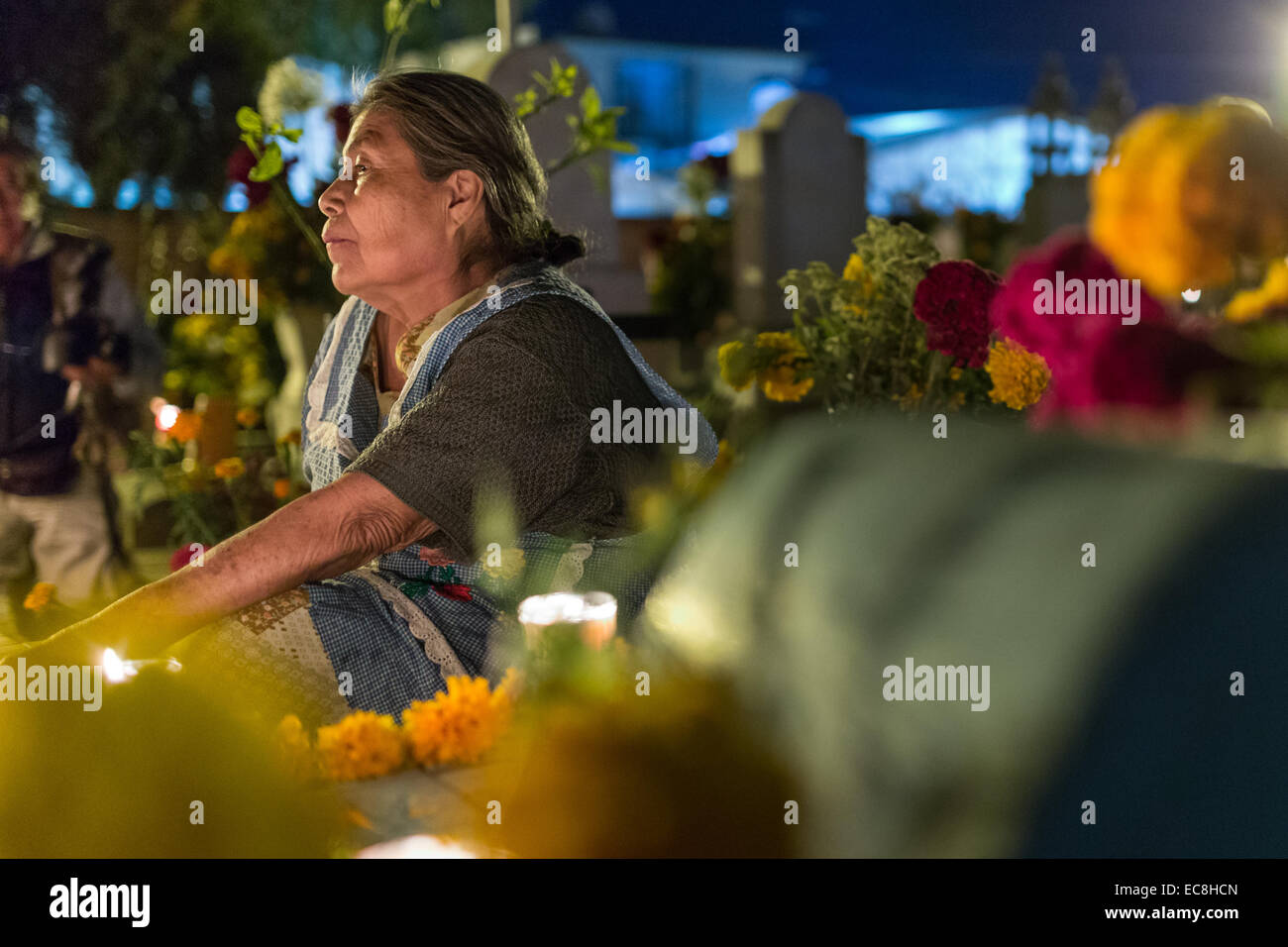 An elderly woman reflects at the gravesite of a relative at Xoxocatian cemetery decorated with flowers and candles for the Day of the Dead Festival known in spanish as D’a de Muertos on October 31, 2014 in Oaxaca, Mexico. Stock Photo