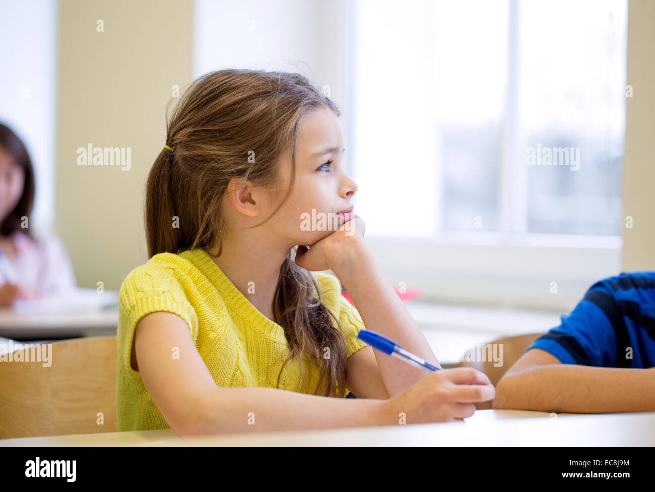 school girl with pen being bored in classroom Stock Photo