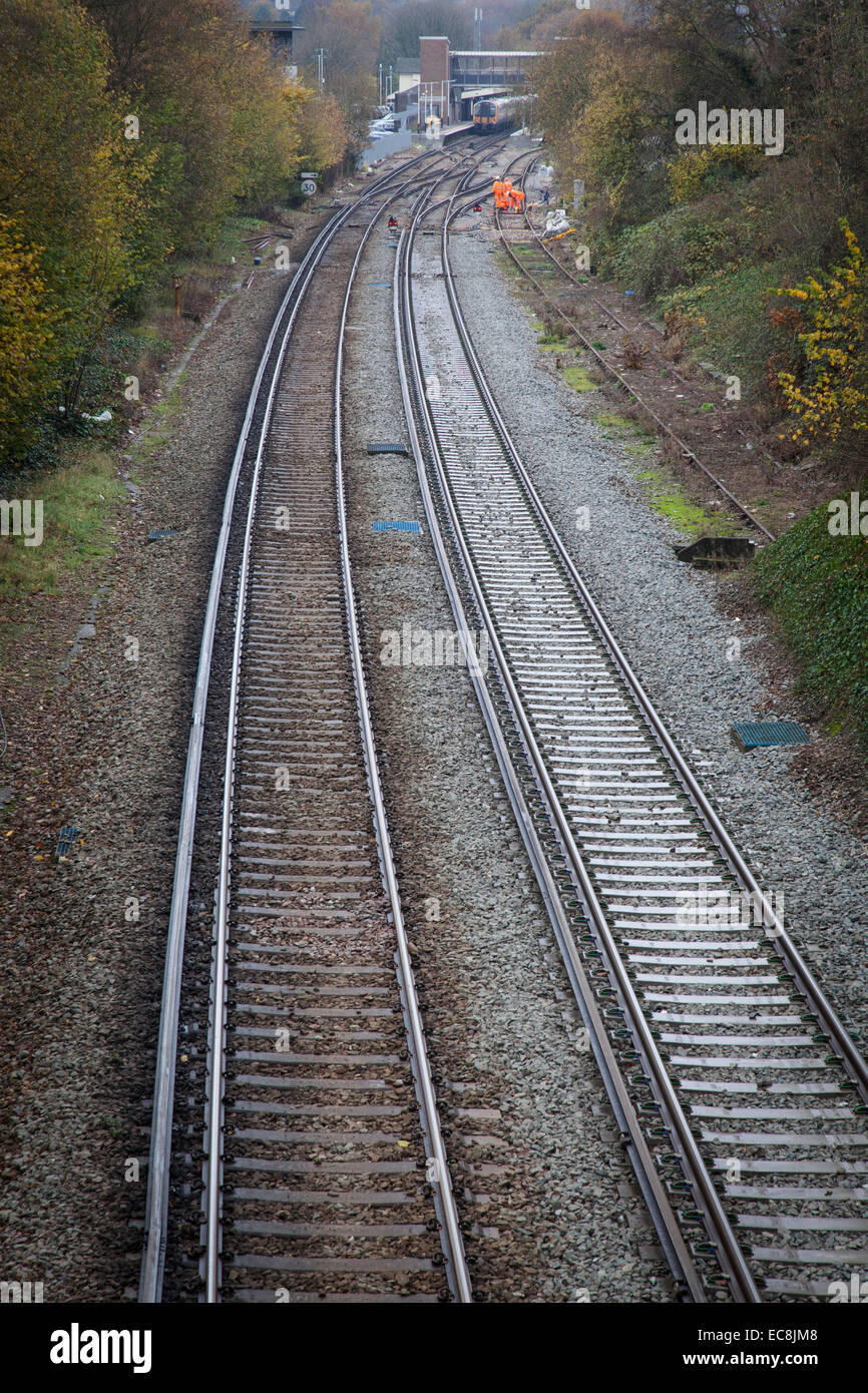 Railway tracks curve past workers in hi-viz suits towards the distant station platform of Haslemere. Stock Photo