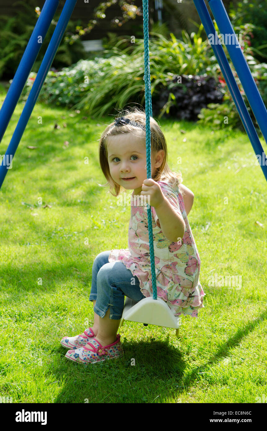 Girl, two years old, sitting on swing in garden. Summer. England, UK