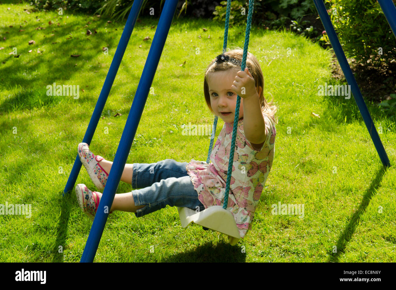 Girl, two years old, sitting on swing in garden. Summer. England, UK