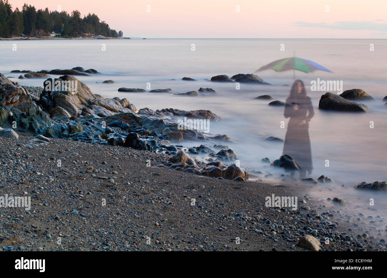 Long exposure of a ghostly image of woman with umbrella on the beach in Sechelt, BC, Canada Stock Photo