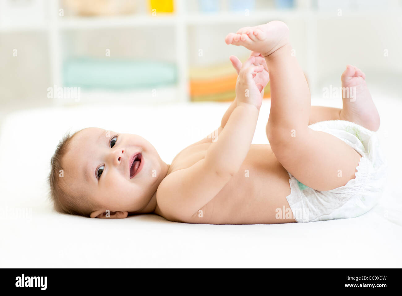 baby boy lying on white sheet and holding his legs Stock Photo