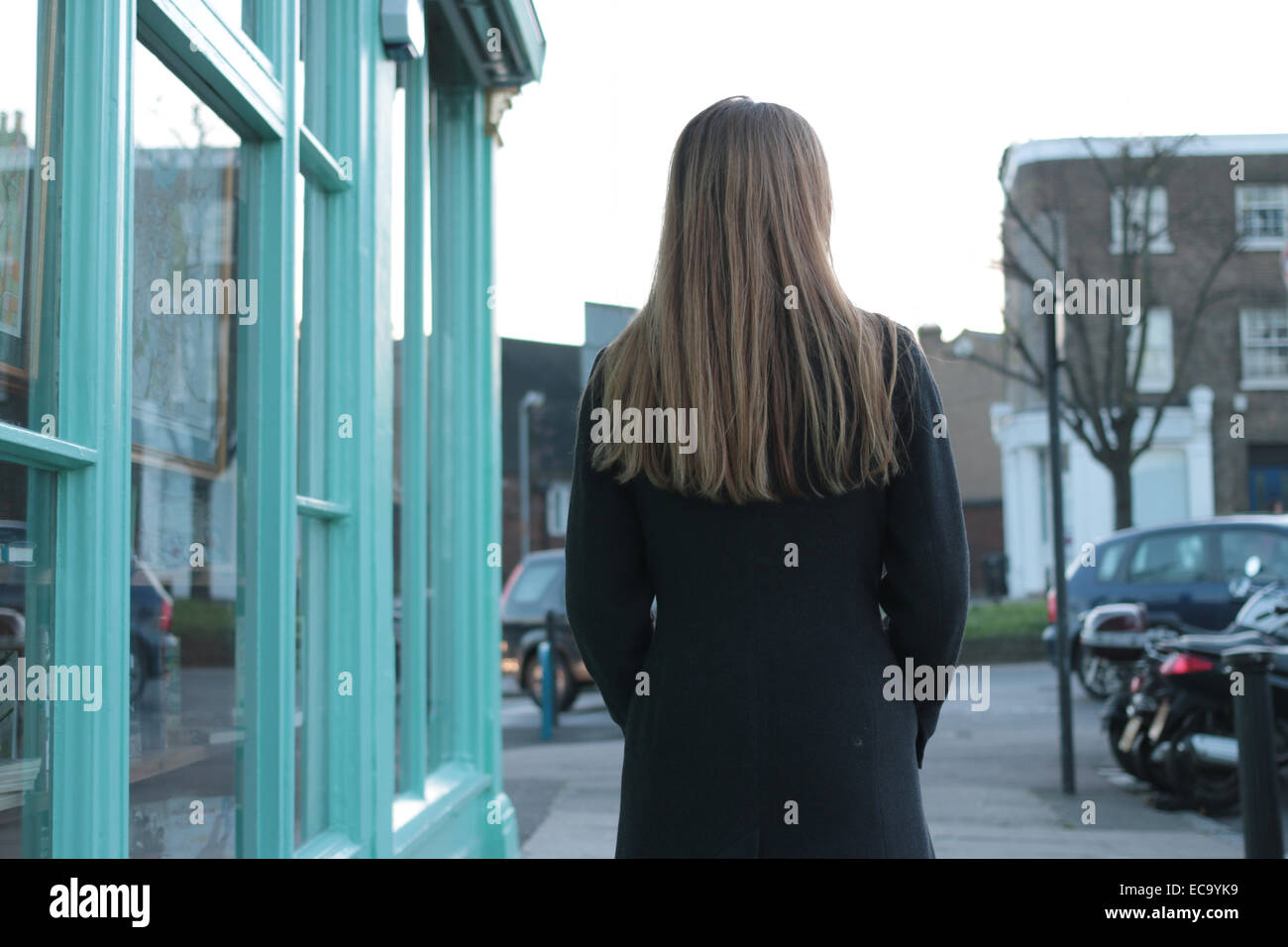 Rear view shot of a young woman walking past a village shop. Stock Photo