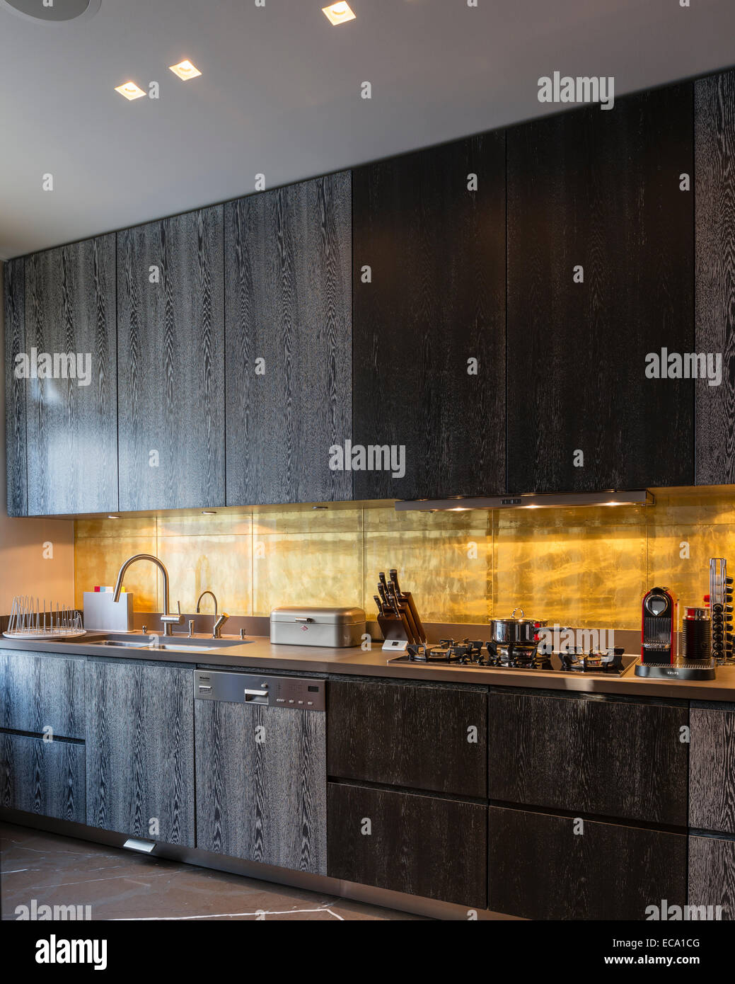 Gold-leaf backsplash in kitchen with dark smoky oak cabinetry Stock Photo