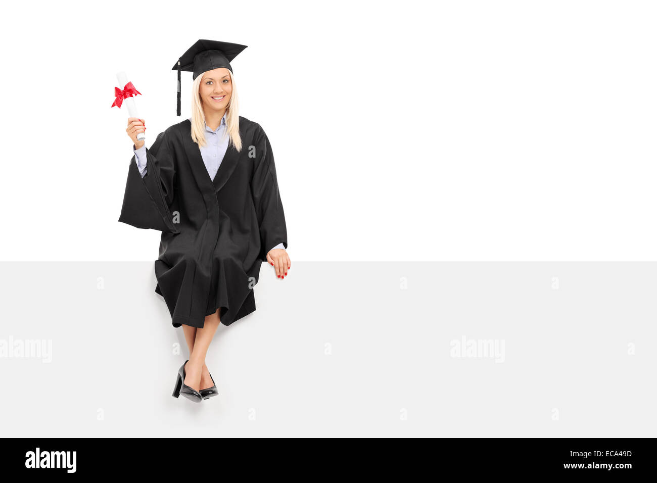 Happy female graduate student holding a diploma seated on a blank panel ...