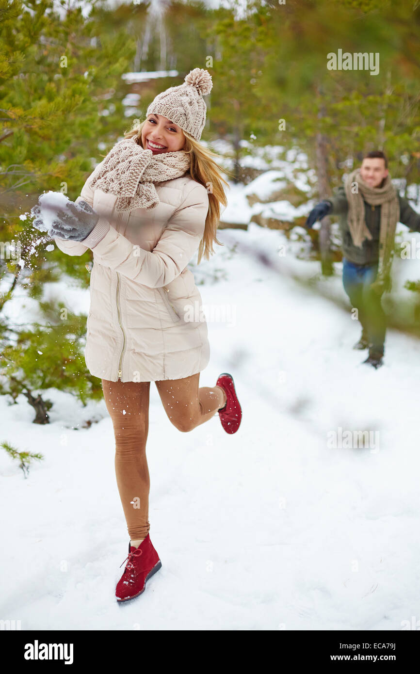 Joyful girl with snowball running in winter forest with her boyfriend ...