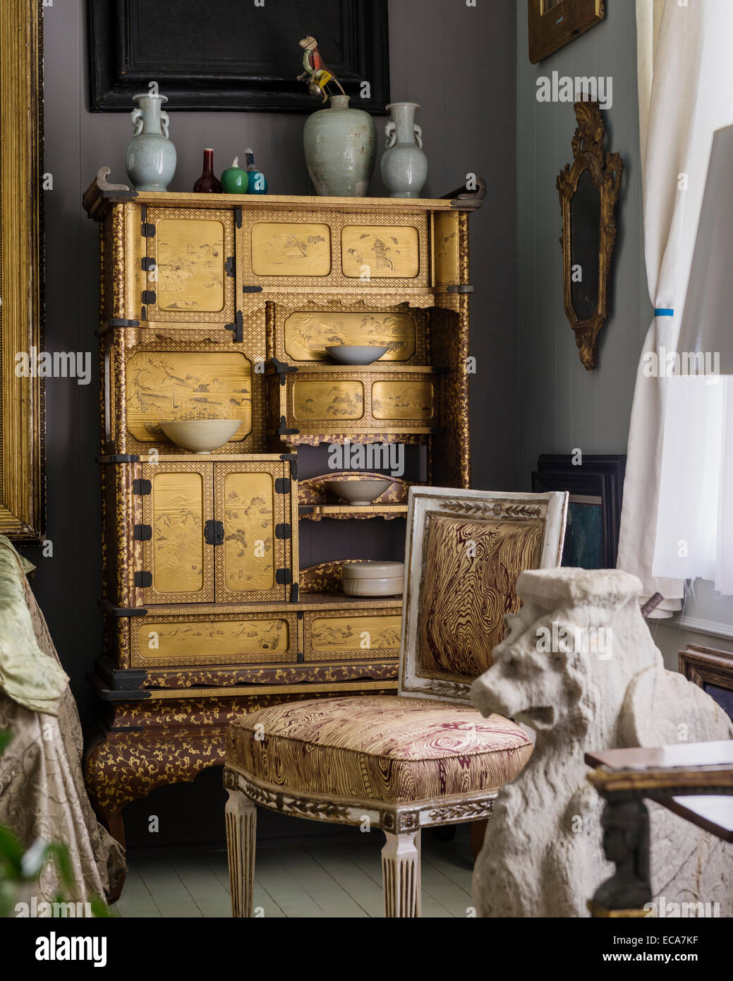 19th century gold and brown Japanese lacquer cupboard in corner of room. In the foreground is one of a pair of Trapezophoros Stock Photo