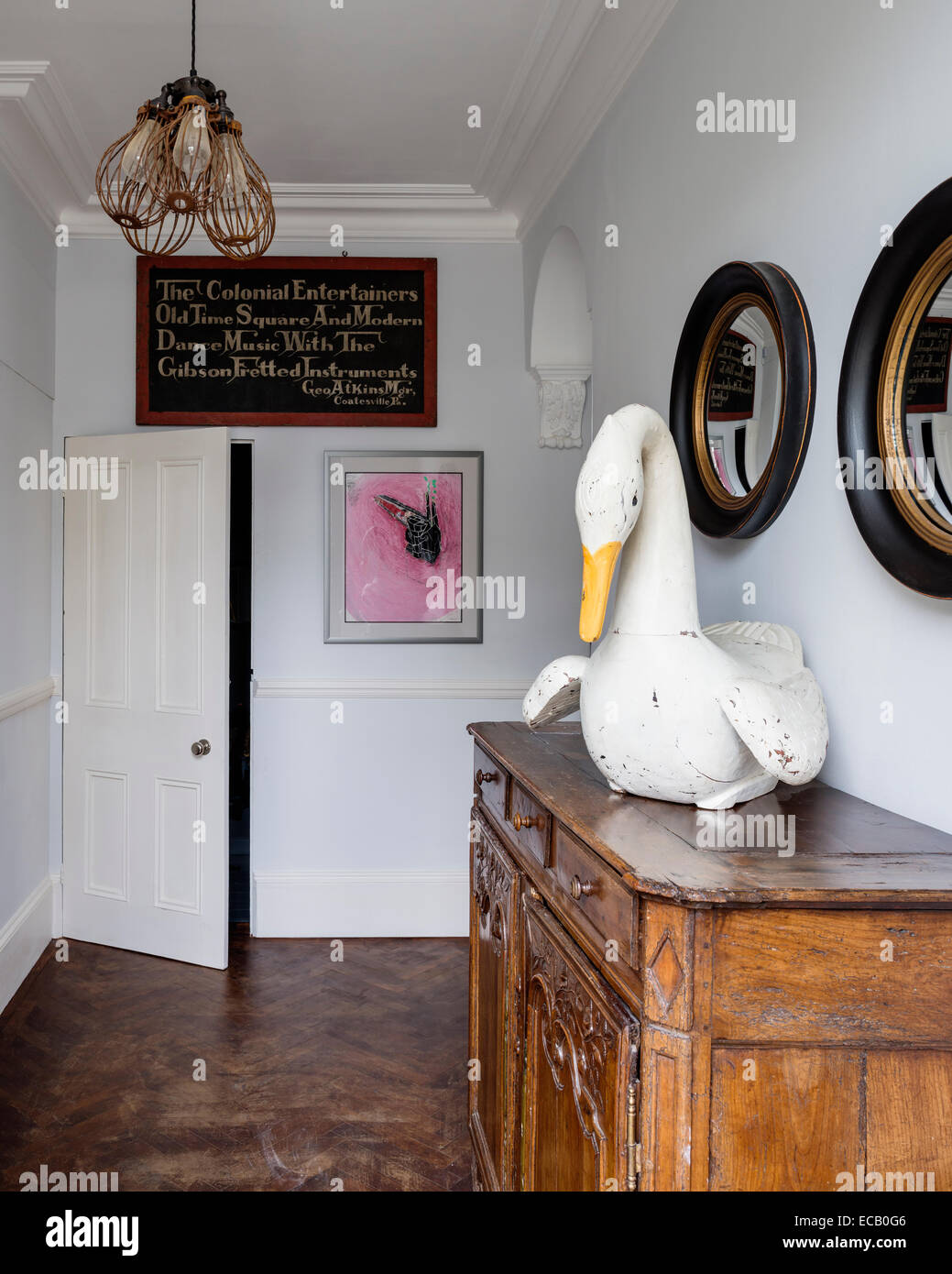 Painted wooden swan from I&JL Brown on French Provencal chest in hallway with rosewood parquet flooring. The lights come from Hi Stock Photo