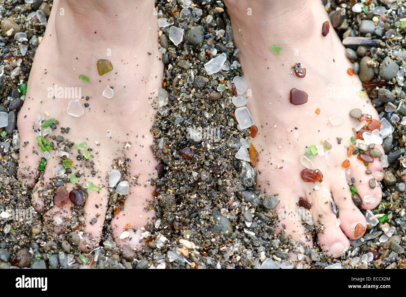 A mans feet are covered in glass from the handfuls of beach glass that