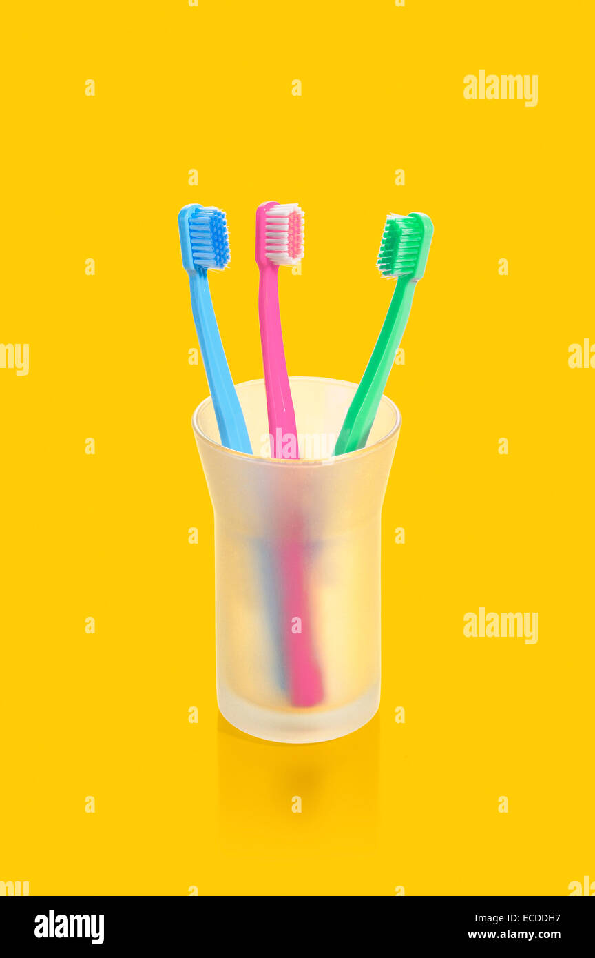 Three toothbrushes in glass on yellow background Stock Photo - Alamy