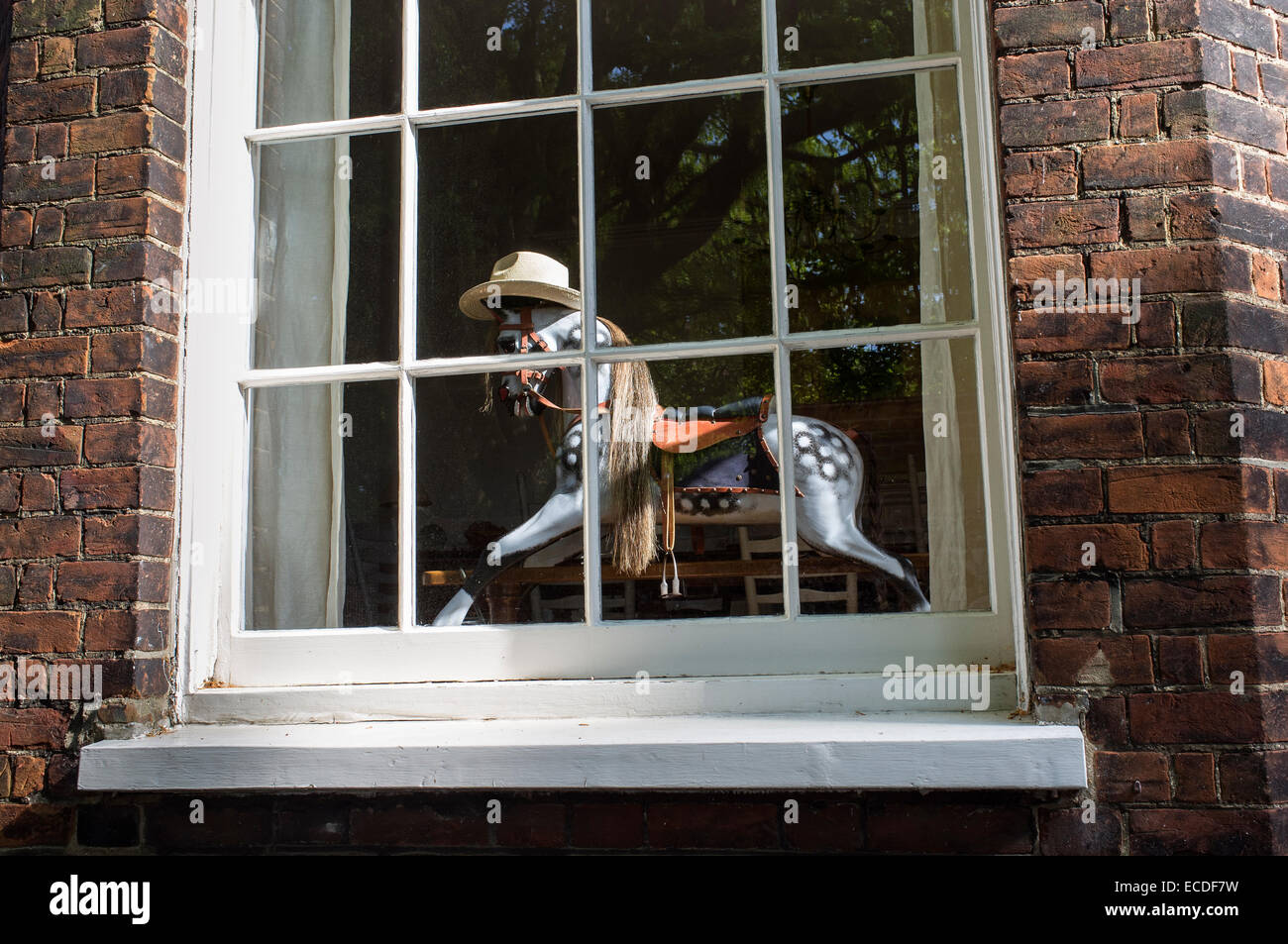 Rocking Horse Wearing Straw Hat in Window of House Stock Photo