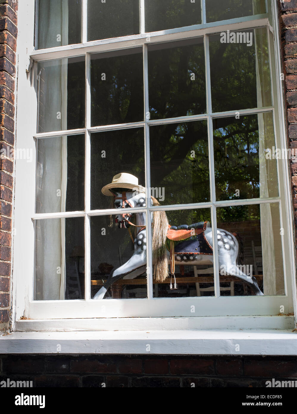 Rocking Horse Wearing Straw Hat in Sash Window of House Stock Photo