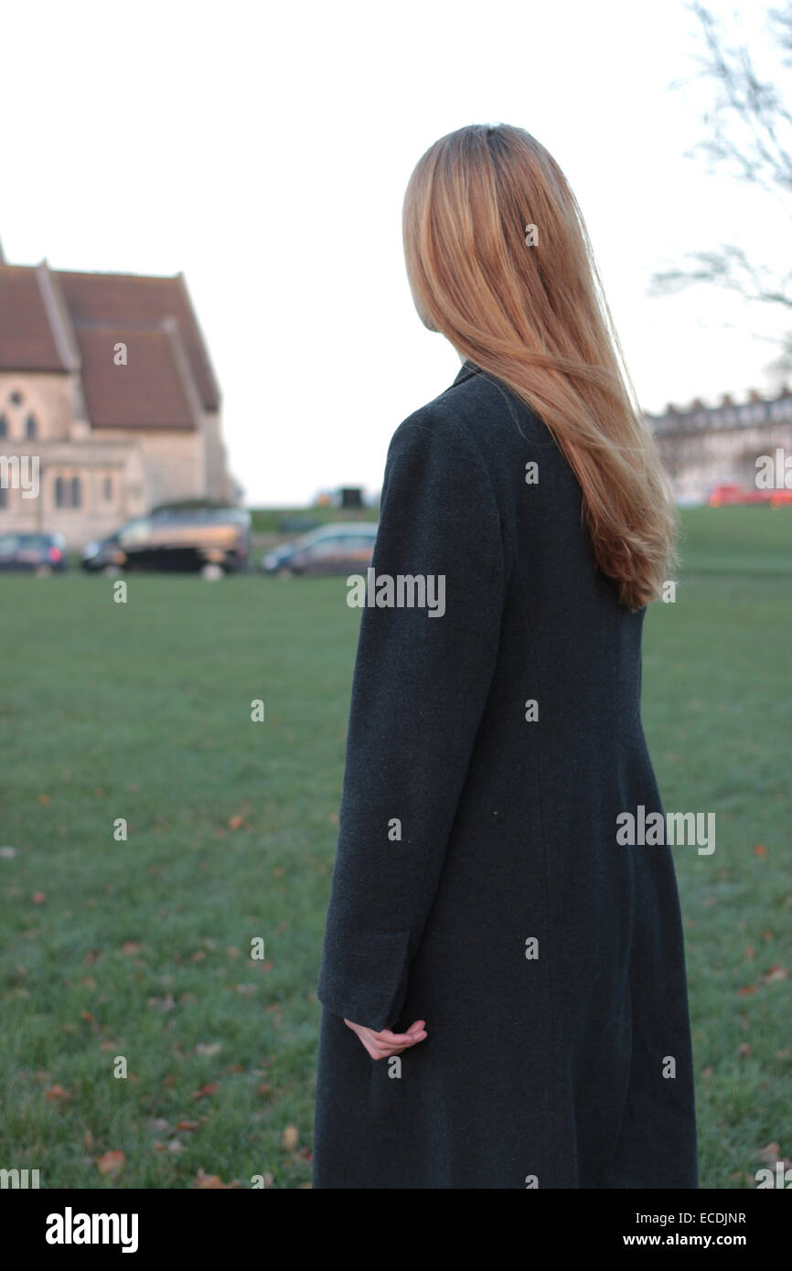 Rear view shot of a young woman standing looking into the distance in a park and a corner of a church. Stock Photo