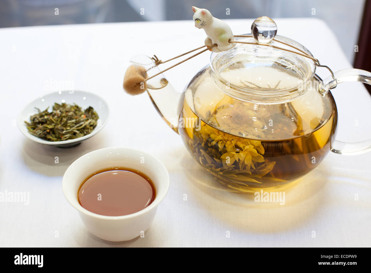 Cup of tea, loose leaf tea, and glass tea pot on white tablecloth Stock