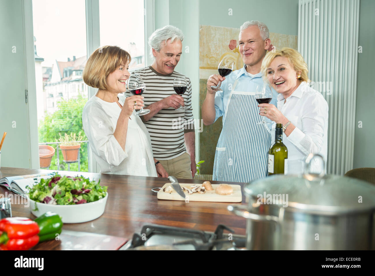 Four senior friends kitchen cooking drinking wine Stock Photo Alamy