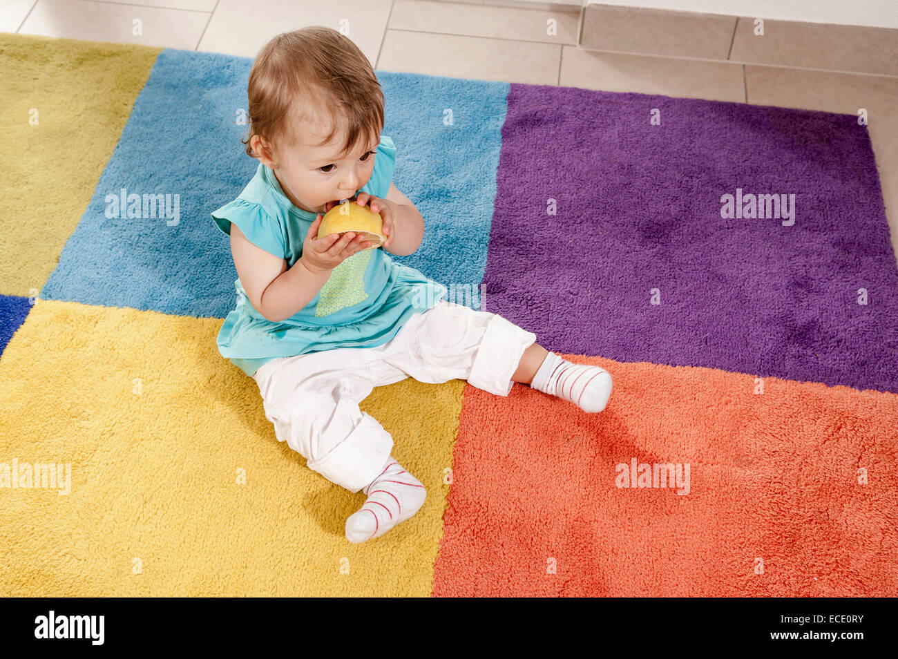 Baby girl 1 year old eating orange carpet Stock Photo
