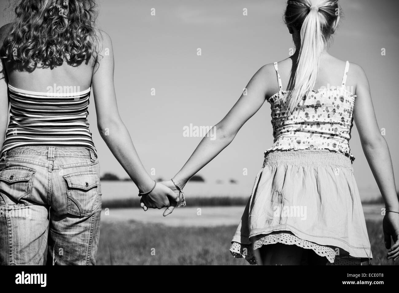 Two girls (10-11) (12-13) hand in hand in field, rear view Stock Photo