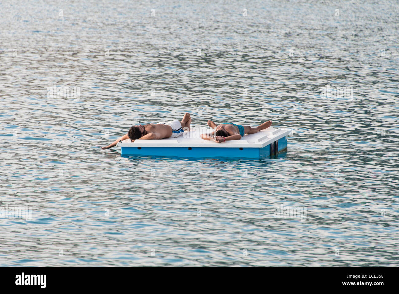 Two men lying on a floating platform in the sea, Italy Stock Photo