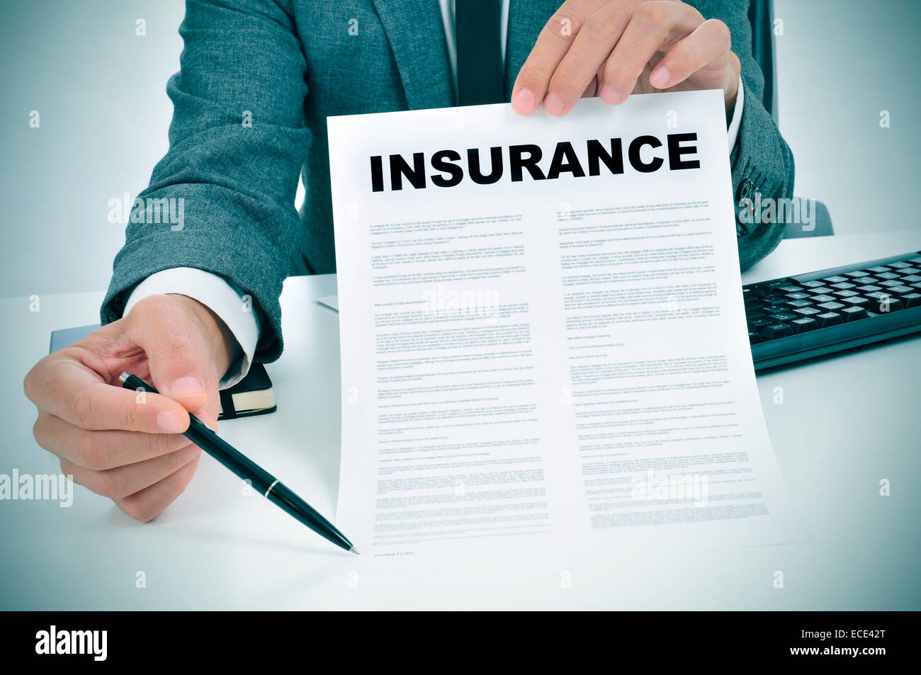 a young man in suit in his office showing an insurance policy and pointing with a pen where the policyholder must to sign Stock Photo