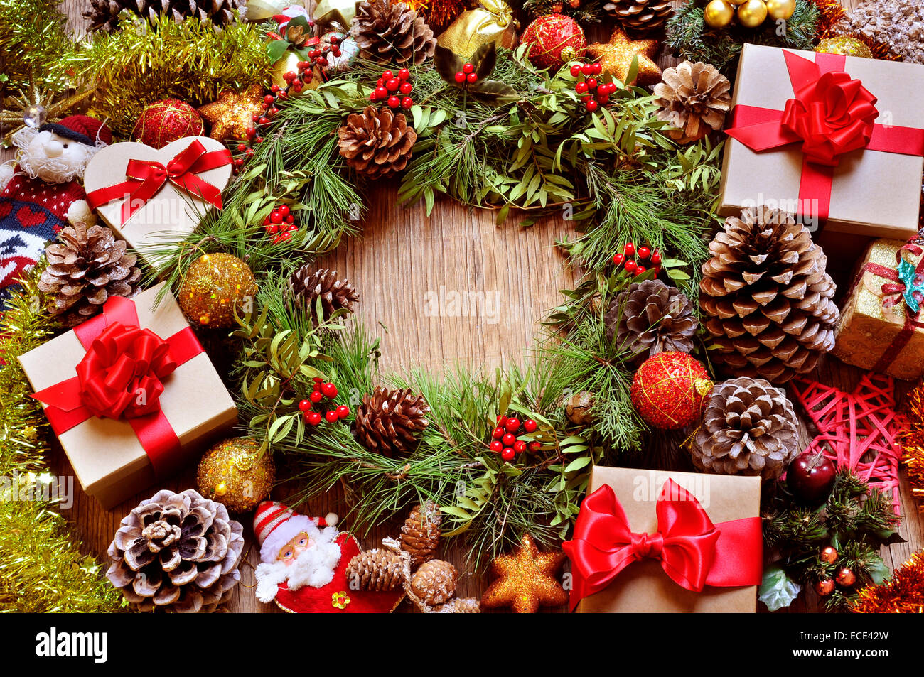 a rustic wooden table full of gifts, and christmas ornaments, such as a natural wreath with branches, berries and pine cones, or Stock Photo