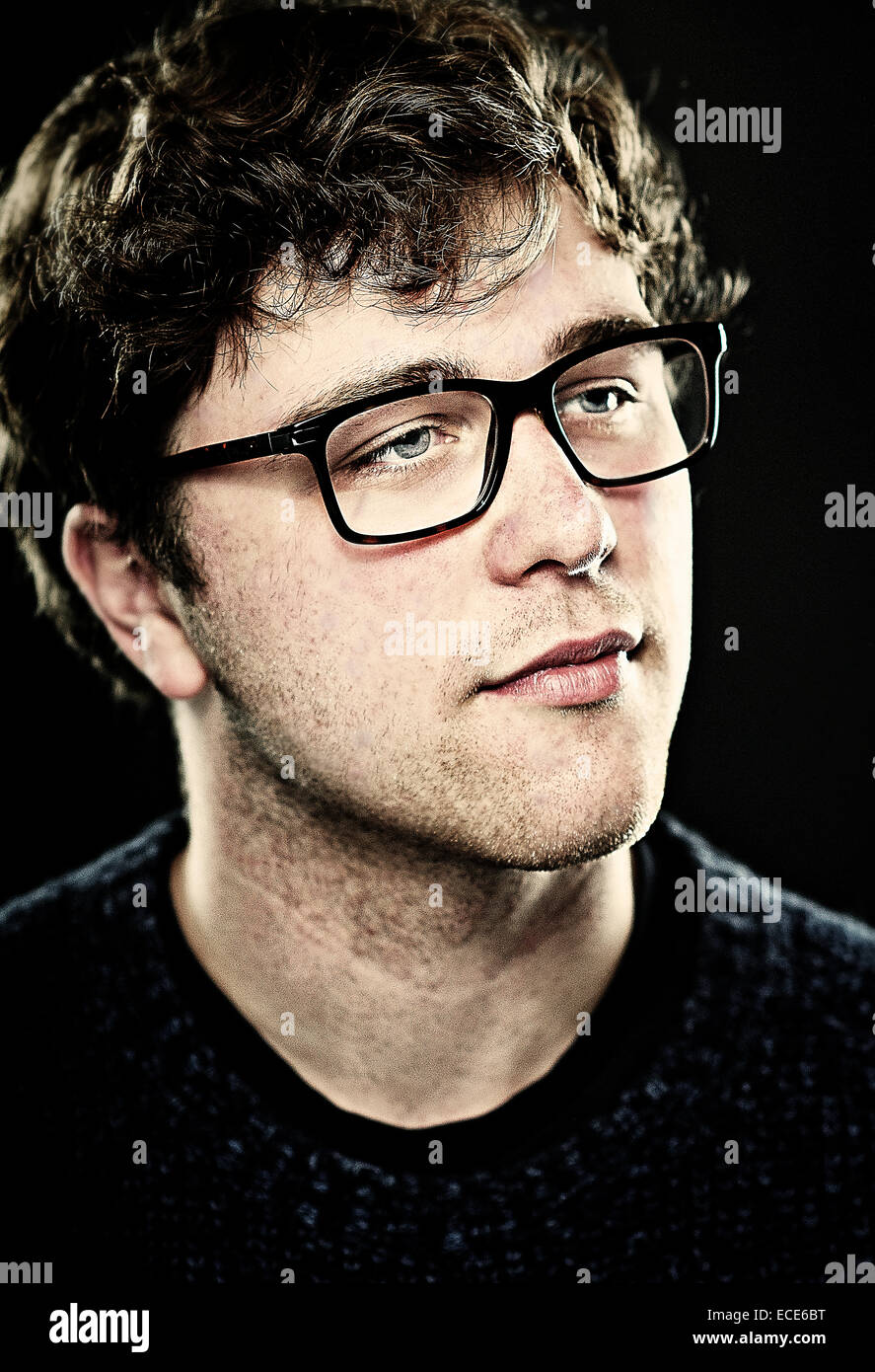 A white European male teenager age 19 wearing glasses. The image is a portrait shot in a studio in color. Stock Photo