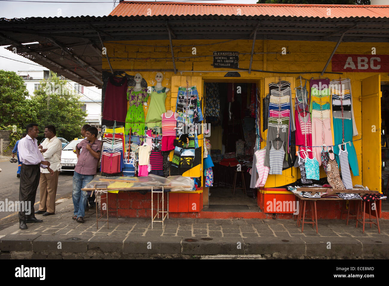 Mauritius, Mahebourg, Central Market, clothing displayed outside corner shop with men outside Stock Photo