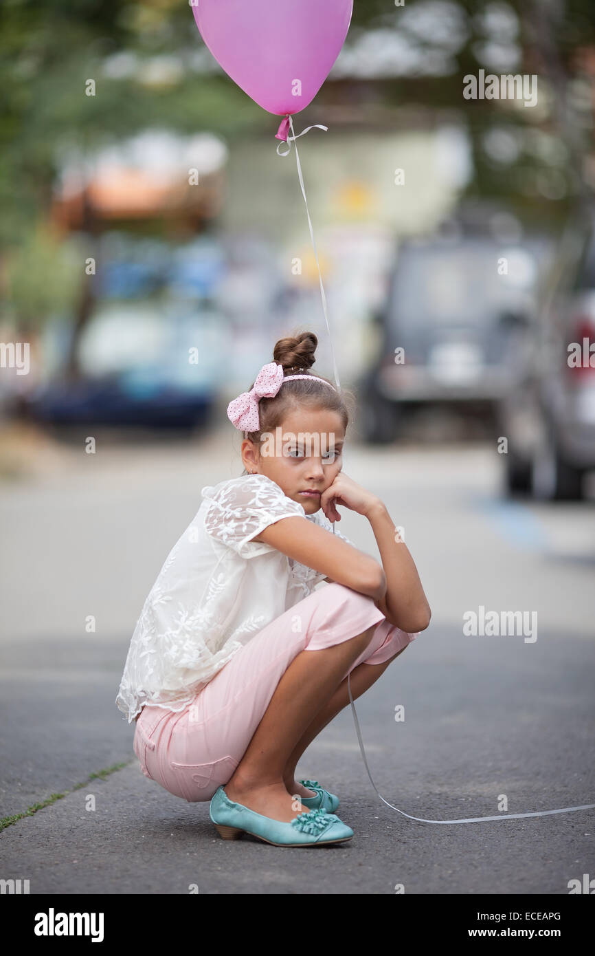 Sad girl (8-9) holding pink balloon Stock Photo
