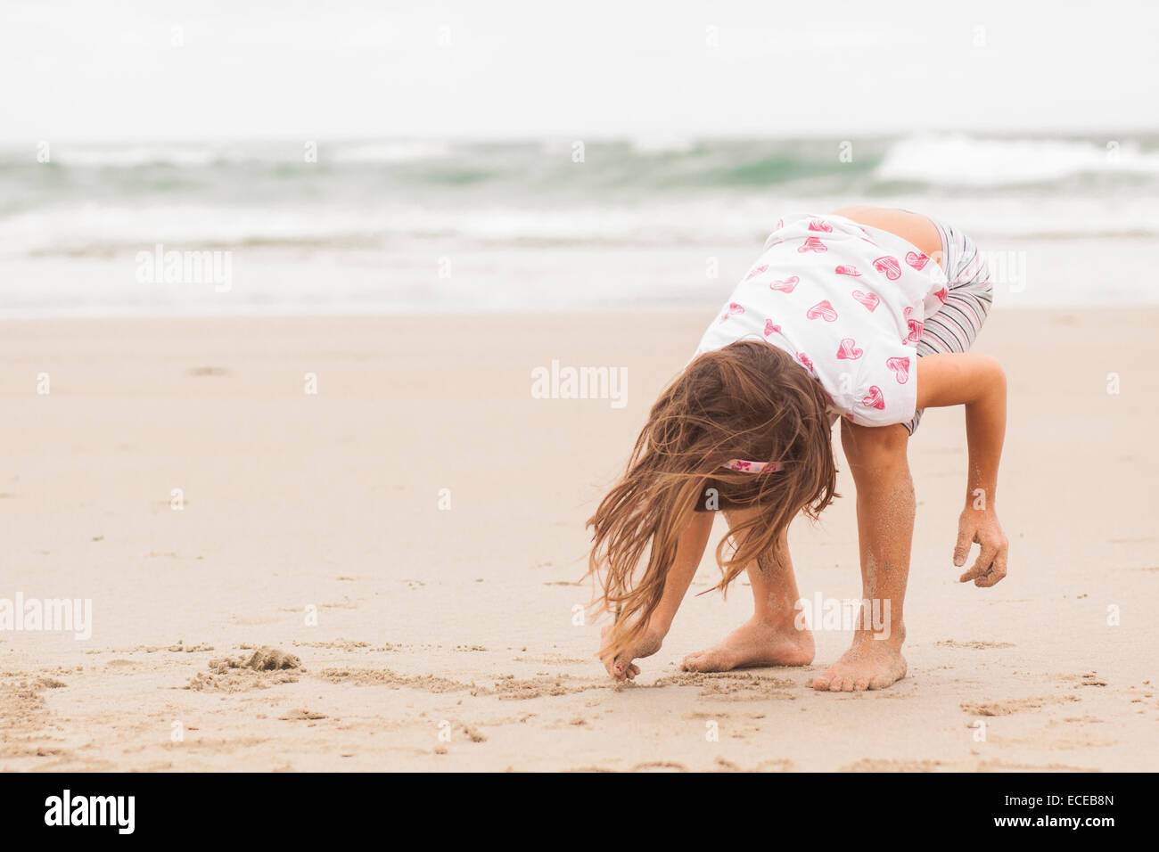 Girl standing on a beach drawing in the sand Stock Photo
