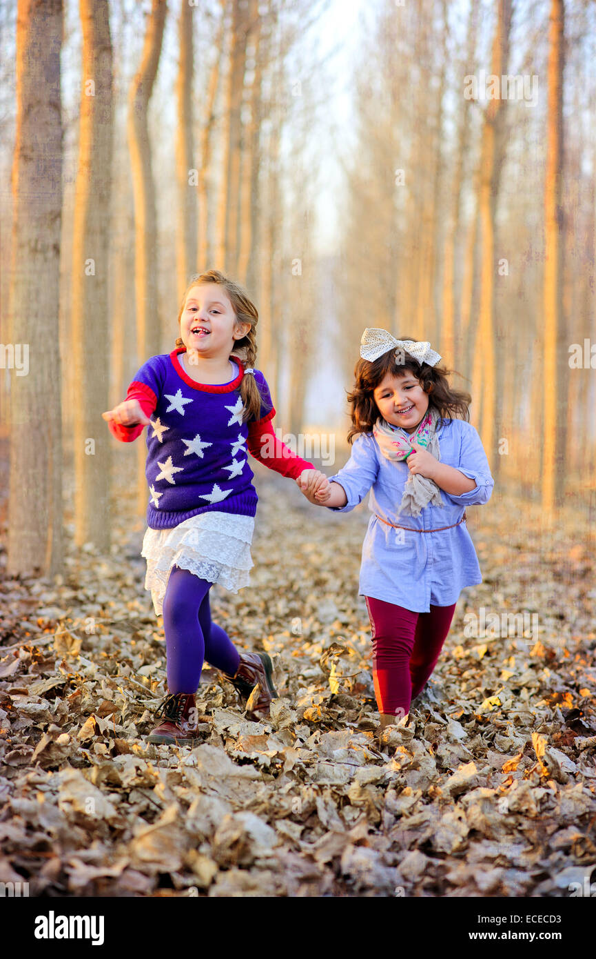Two girls in park holding hands and running in dry leaves Stock Photo