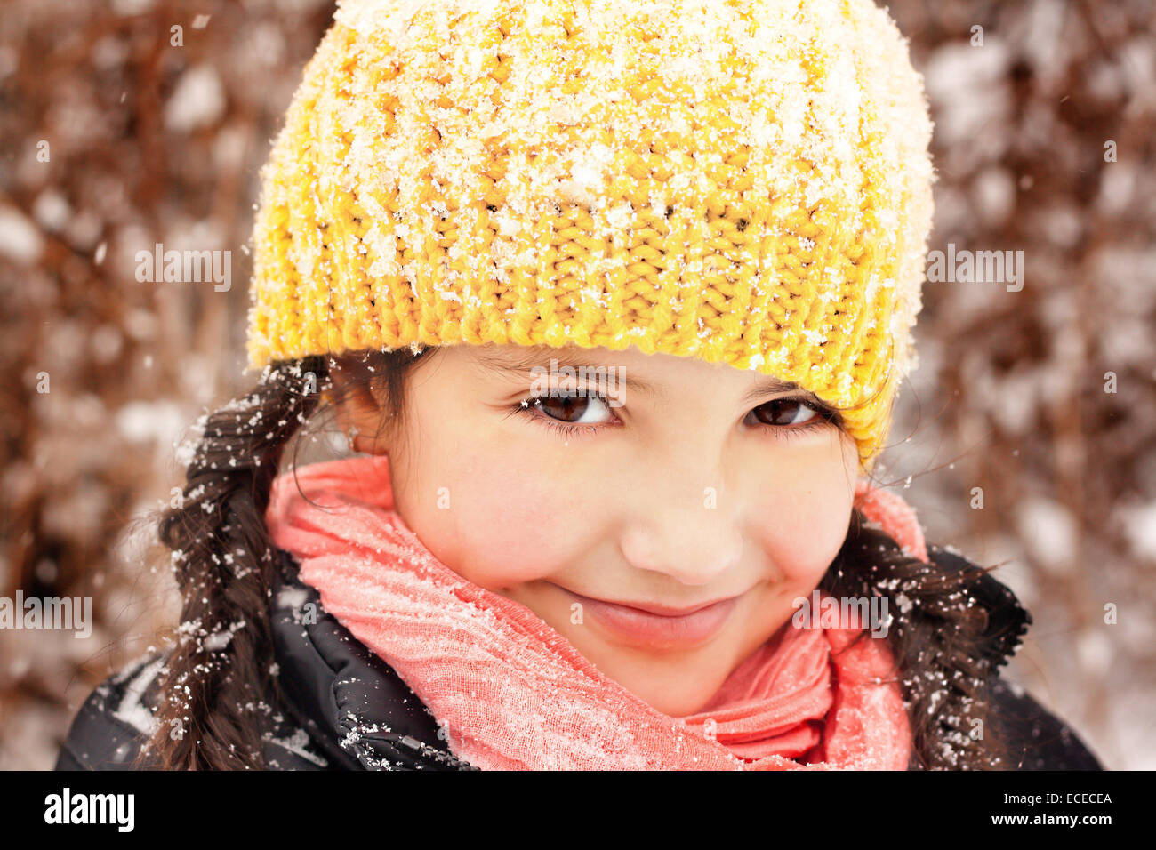 Pretty little girl (6-7) in braids and hat, smiling during snow fall Stock Photo