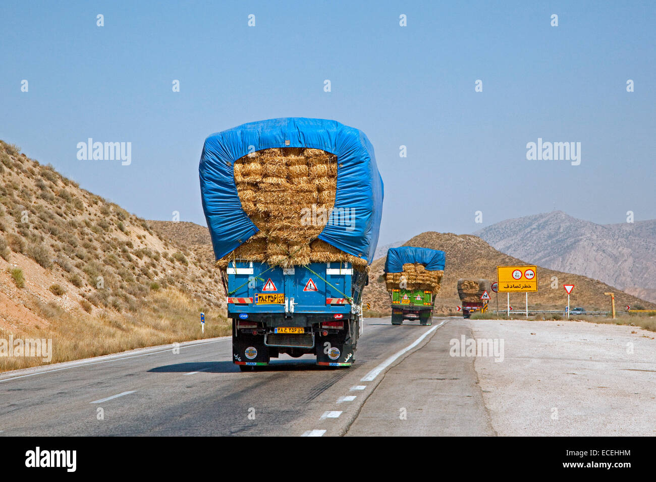 Convoy of heavily loaded trucks transporting bales of hay over highway in Iran Stock Photo