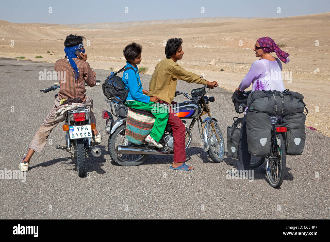 Iranian boys on motorbikes talking to female Western touring cyclist in Iran, close to the Turkmenistan border in Karakum desert Stock Photo