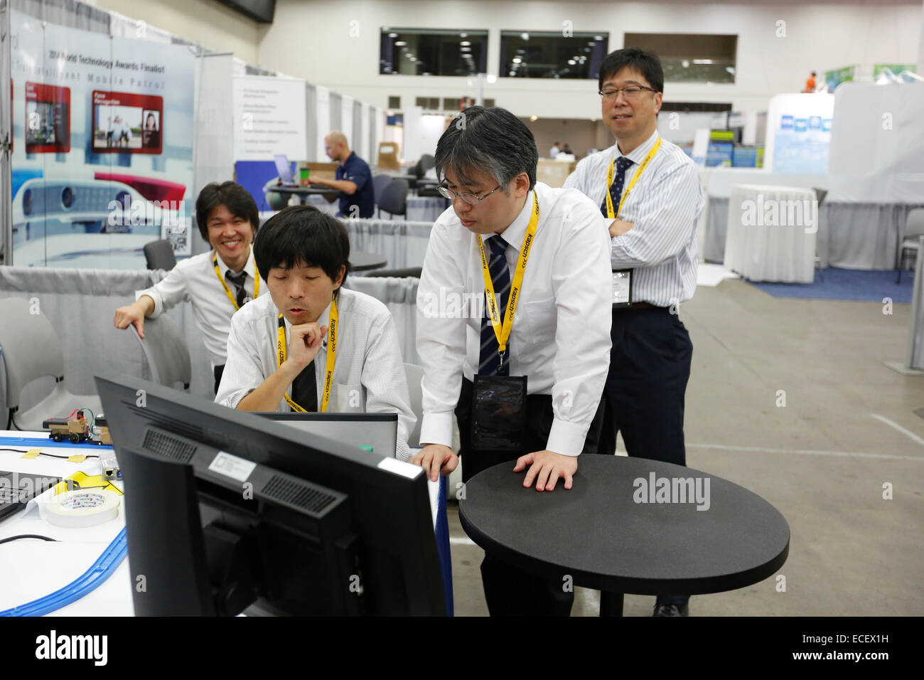 Japanese employees huddle around a computer as they prepare an exhibit for the Intelligent Transport Systems World Congress. Stock Photo